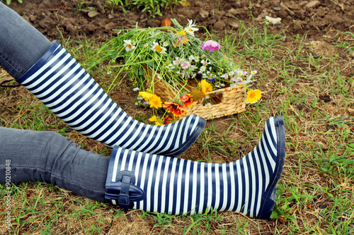 Young woman in rubber boots sitting on meadow outdoors