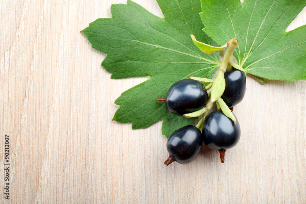Pile of black currants with green leaves on wooden background Pile of black currants with green leaves on wooden background