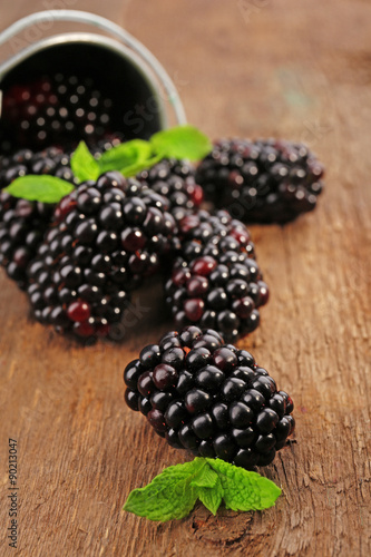 Ripe blackberries with green leaves on wooden table, closeup