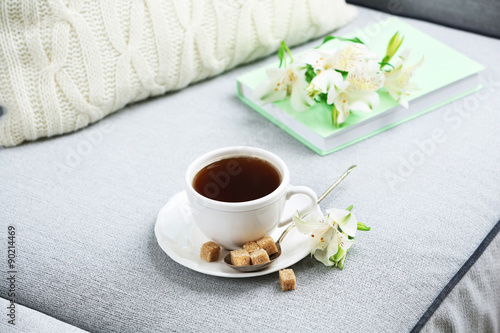 Cup of coffee with lump sugar and flowers on sofa