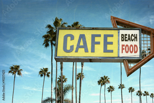 aged and worn vintage photo of cafe sign on beach with palm trees