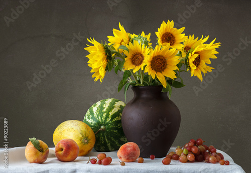 Fototapeta Naklejka Na Ścianę i Meble -  Букет подсолнухов в глиняном кувшине и фрукты на столе.