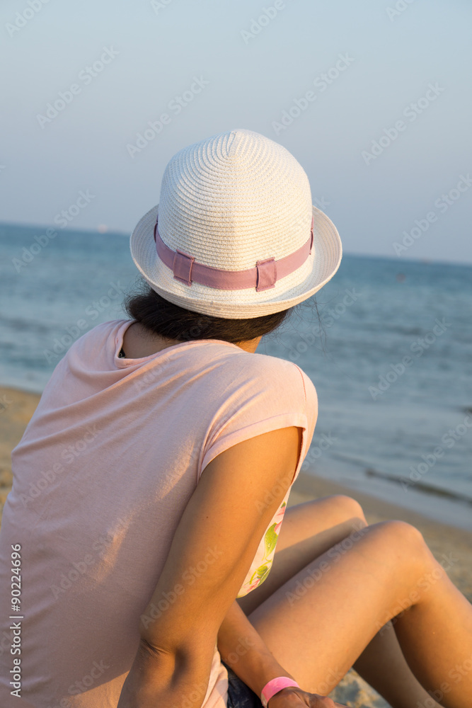 Girl brunette in white hat looking at sea while sitting on beach