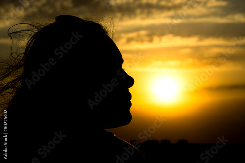 Young girl face silhouette looking on beautiful cloudy sky with golden sunset