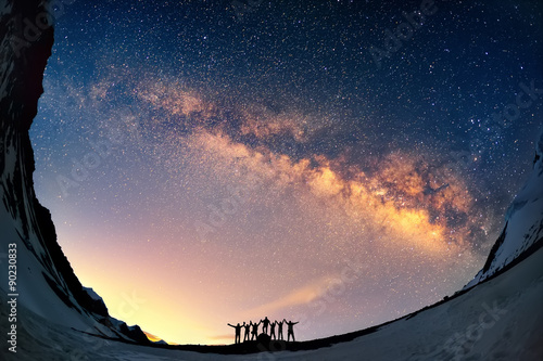 Teamwork and support. A group of people are standing together holding hands against the Milky Way in the mountains. 