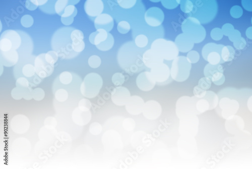 Bokeh blurry winter holidays background in blue and white. Blurry sparkling lights; snowfall.