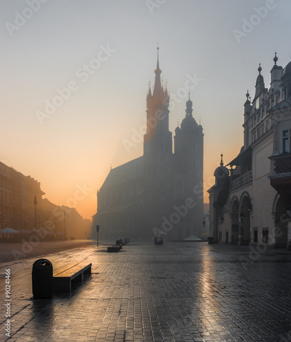 Krakow, Poland, St Mary's church and Sukiennice (Cloth hall) on the Main Market Square in morning fog illuminated by rising sun