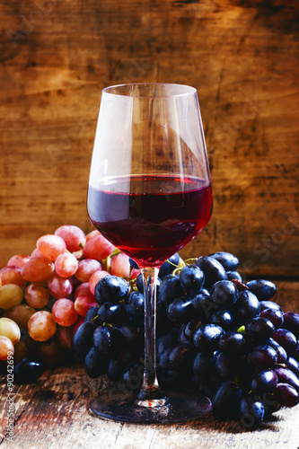 Red wine and blue and pink grapes on a dark wooden background, t