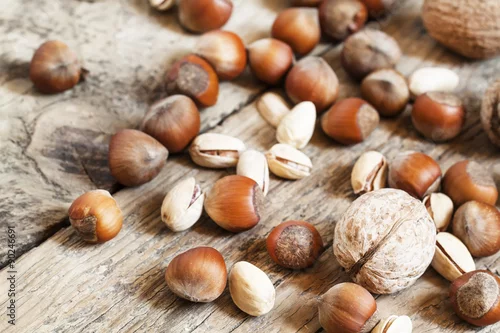 Obraz Orzechy włoskie, orzechy laskowe i pistacje na drewnianym stole, stonowany wizerunek