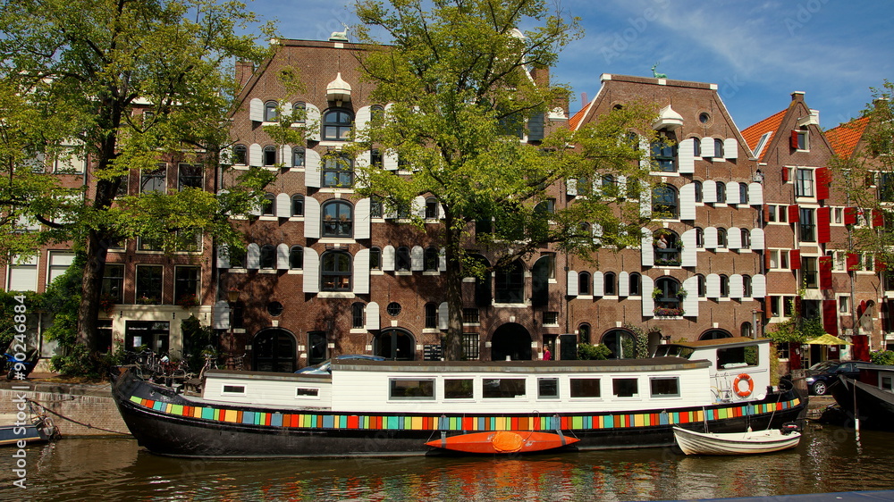buntes Hausboot ankert auf Gracht vor Häuserfassaden in Amsterdam