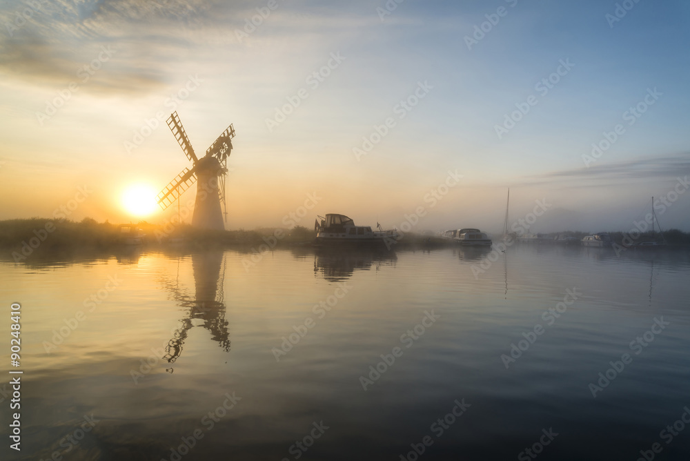 Stunnnig landscape of windmill and river at dawn on Summer morni
