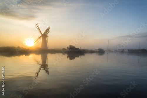 Stunnnig landscape of windmill and river at dawn on Summer morni