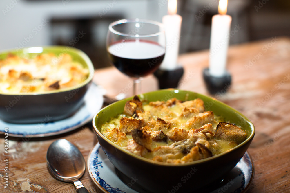 A bowl of soup with cheese and bred crumbs, with a glass of whine and candles