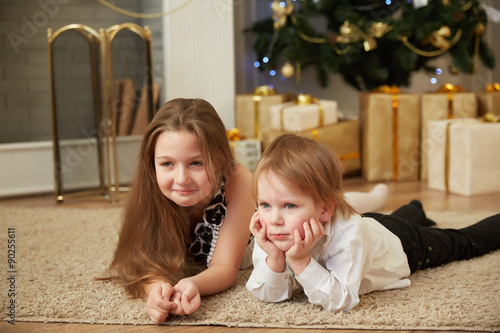 Cheerful girl and boy lying on the floor near a Christmas tree