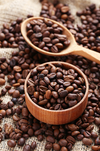 Coffee beans in wooden spoon and bowl on a sack, close up