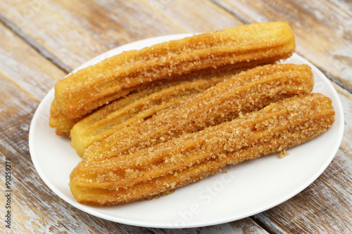 Churros on white plate on rustic wooden surface 