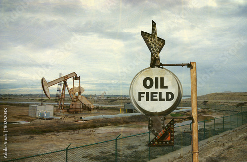 Photography aged and worn vintage photo of oil field sign with derrick in background