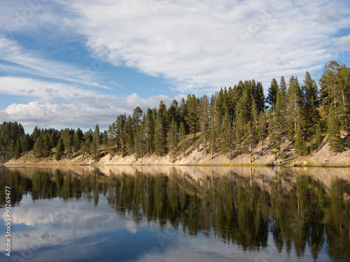 Fototapeta Naklejka Na Ścianę i Meble -  Scenic view of the mirror like water surface of the Yellowstone River and partly cloudy blue sky, Yellowstone National Park.