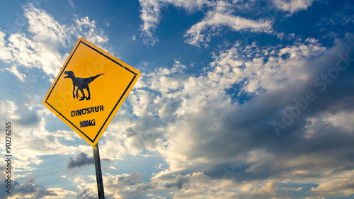 Yellow traffic label with dinosaur pictogram on sky background