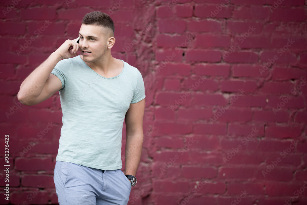 Young man talking on the phone in front of brick wall Young man talking on the phone in front of brick wall
