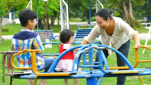 Mother rolls her children on the carousel at the playground in the park 