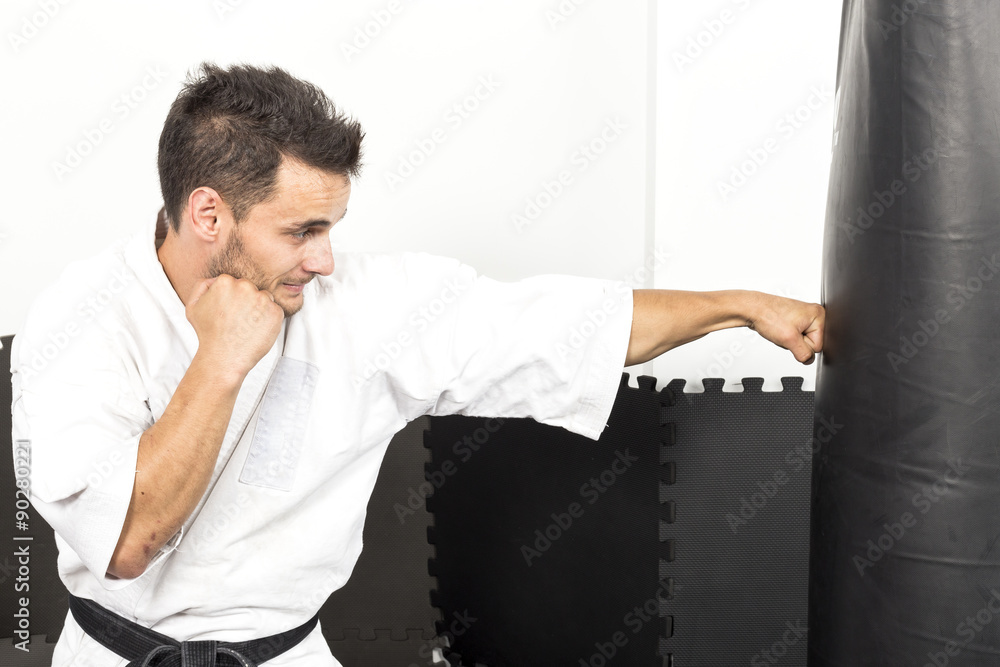 Young man in kimono throwing punches at a heavy punching bag Young man in kimono throwing punches at a heavy punching bag