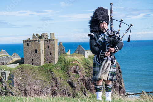 Tablou canvas Traditional scottish bagpiper in full dress code at Dunnottar Castle in Stonehav
