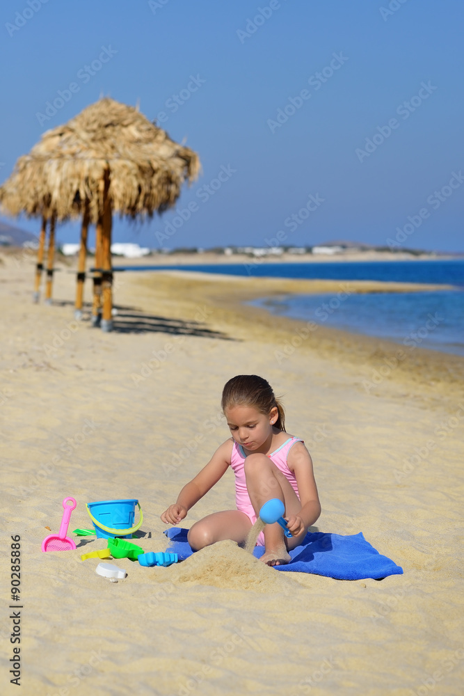 Adorable toddler girl playing with her toys at the beach
