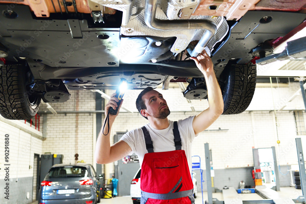 Mechaniker in einer Werkstatt kontrolliert den Unterboden eines Autos ...