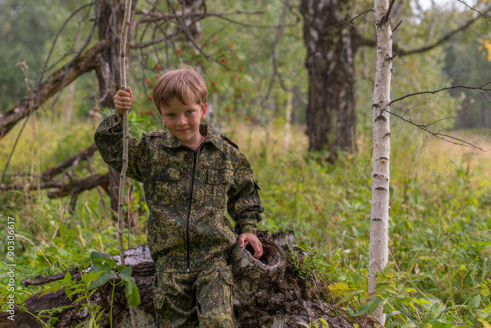 The boy in the autumn forest camouflage with a stick in his hand