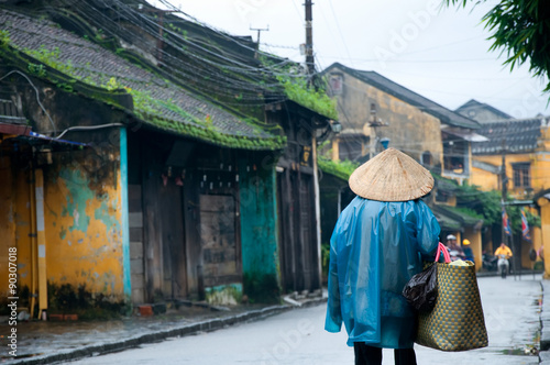 An old woman in traditional vietnamese conical hats walk on a street in Hoi An, Vietnam. Hoi An is a World Heritage Site. © danhvc