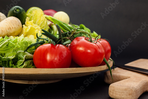 Bowl full of vegetables with a wooden cutting board and knife in the background ,