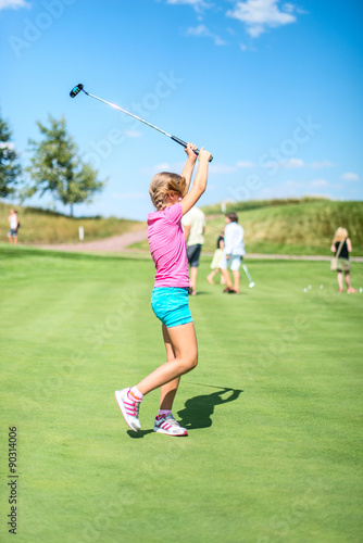 Cute little girl playing golf on a field outdoor. Summertime