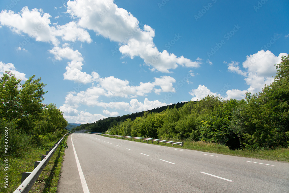Highway through green forest with blue sky background