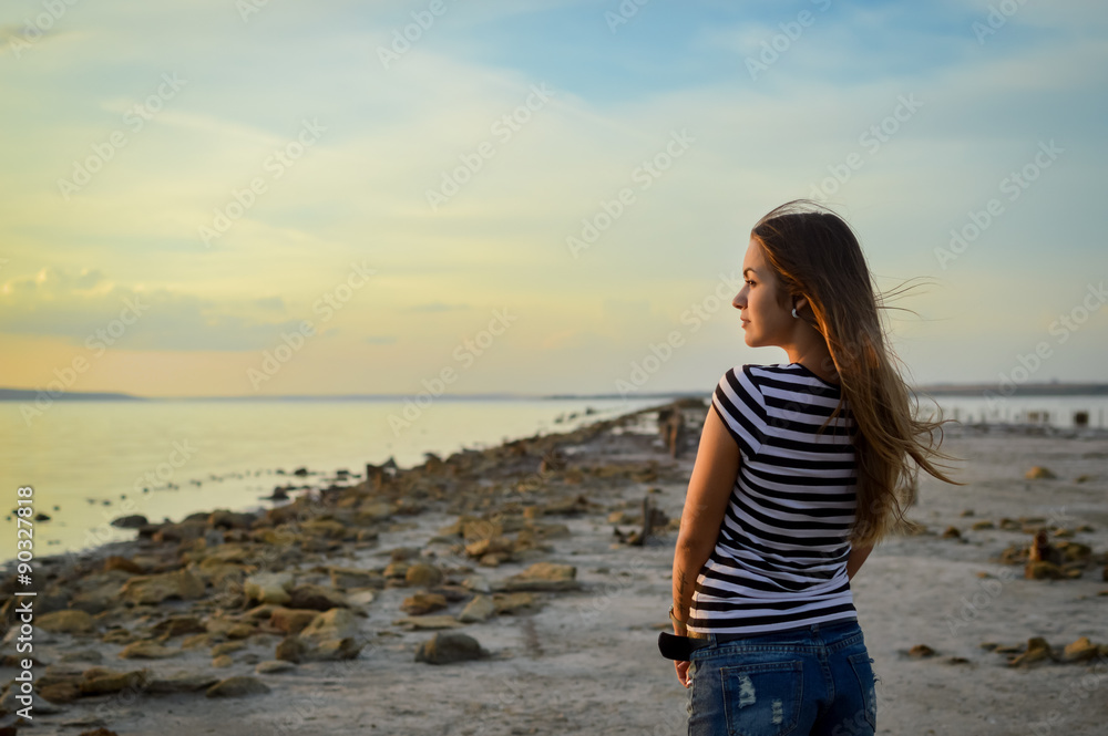 Young woman in striped T-shirt standing on rocky beach 