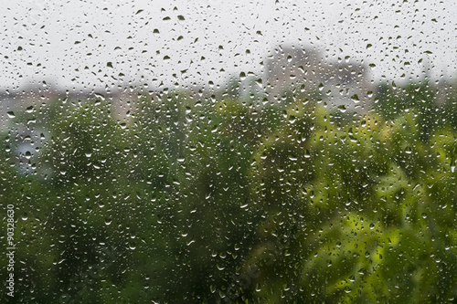 Raindrops on a window pane. Summer day. In the background buildings and trees