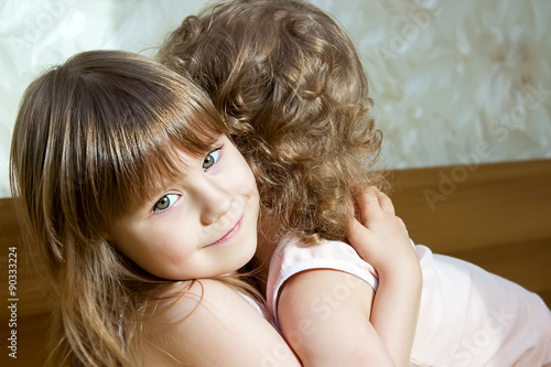 Two adorable little girls hugging each other in the bedroom