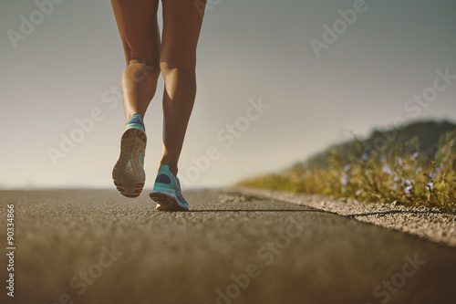 Female runner  feet in running shoes going for a run on the road at sunrise or sunset. Shallow depth of field, low angle, toned colors.