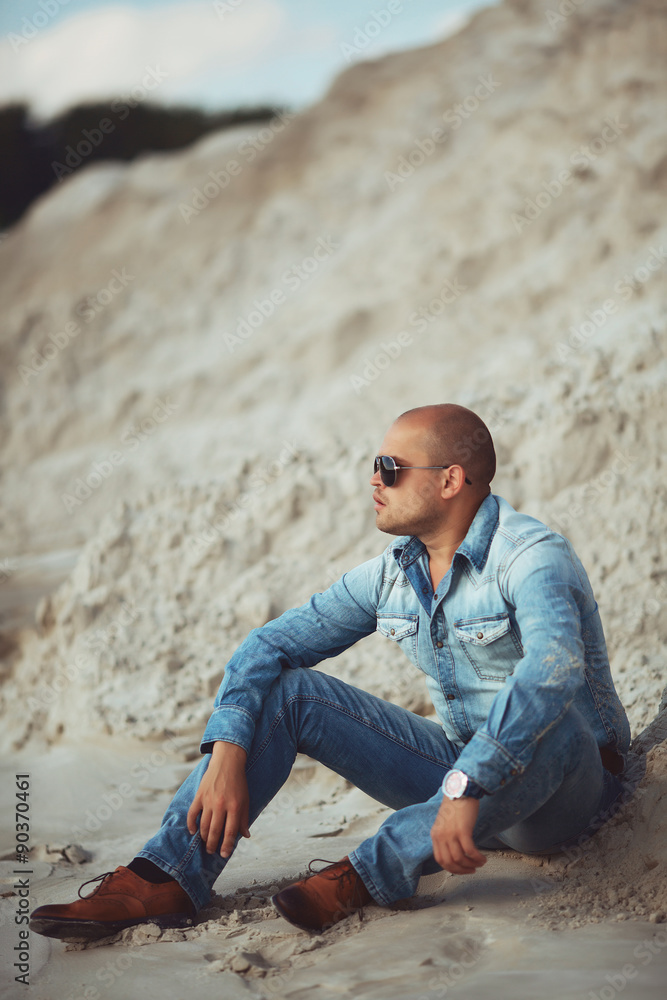 Obraz premium Guy sitting on the sand, a tanned jeans clothes