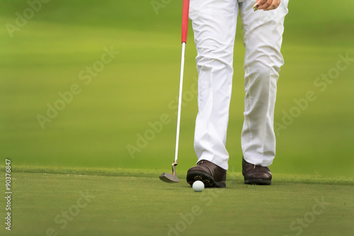 golfers walking on green with putter.