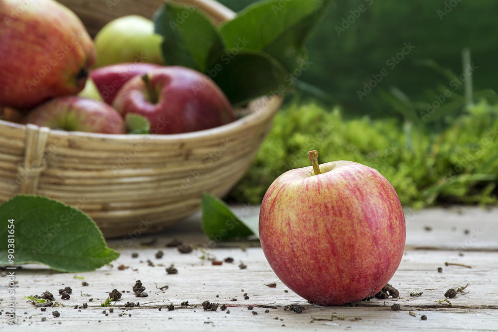 organic apple and a blurred basket with apples on a wooden deck