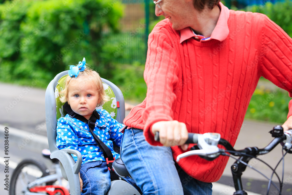 Obraz premium little girl on bike seat cycling with father in the city