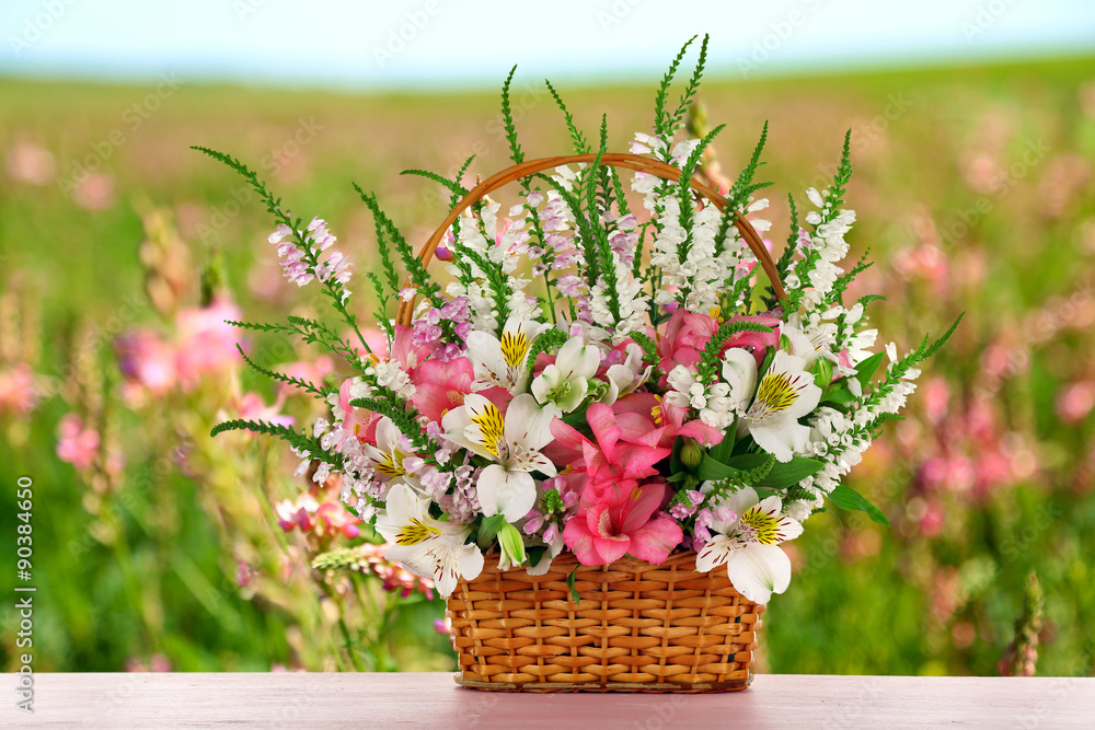 Beautiful wildflowers in wicker basket on field background