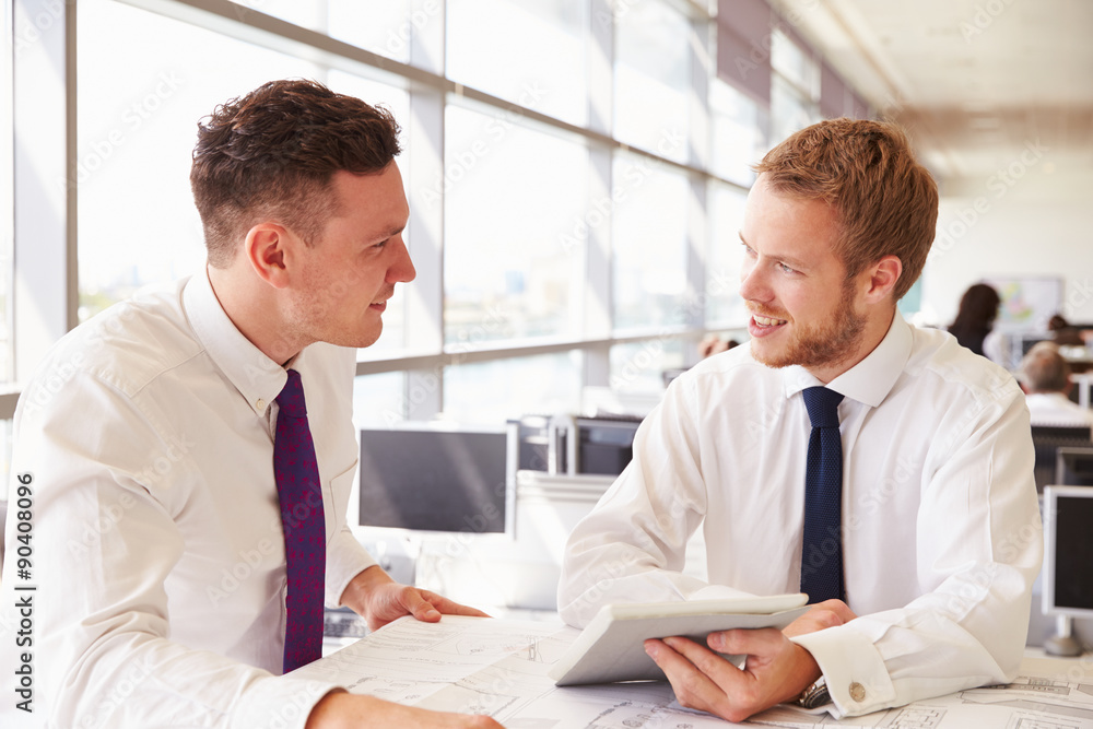 Two young male architects in discussion at an office desk Two young male architects in discussion at an office desk