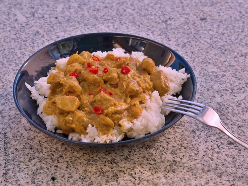 Detailed Picture of typical indian food hot lamb curry with rice and choped chili served on the deep plate or shallow bowl in the gatden on the stone granit table with silver or stainlessteel fork. photo