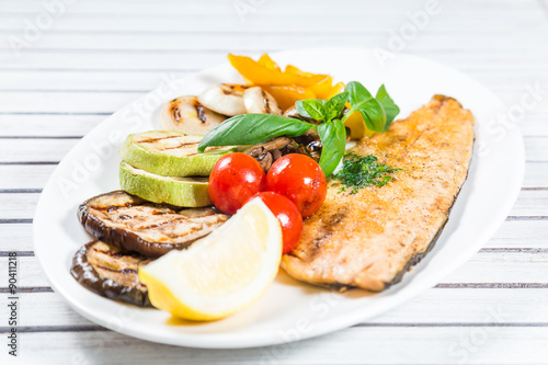 Tasty baked fish with grilled vegetables on plate on wooden table close-up