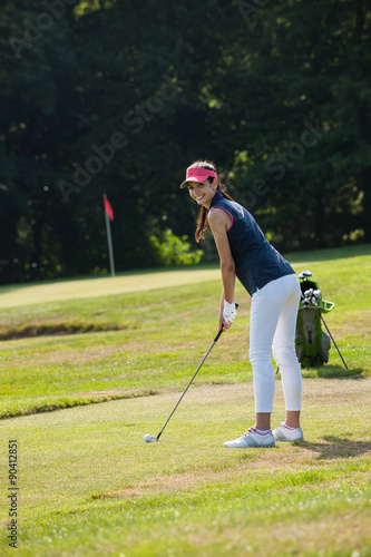 Portrait of a young woman swinging her club on a golf course.