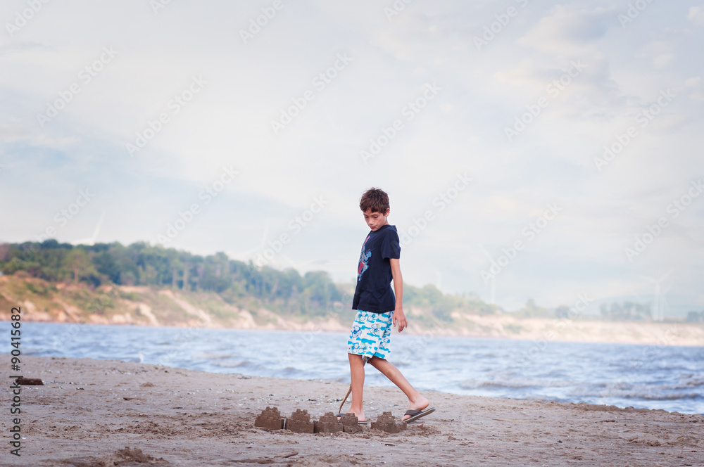 young boy on a sandy beach building sandcastles by the water