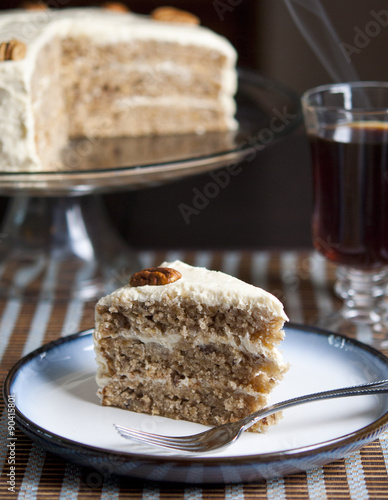 Fototapeta Naklejka Na Ścianę i Meble -  Slice of hummingbird cake with whole cake and coffee in background