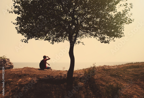 Happy man sitting on hill near tree looking at the sea, sport an